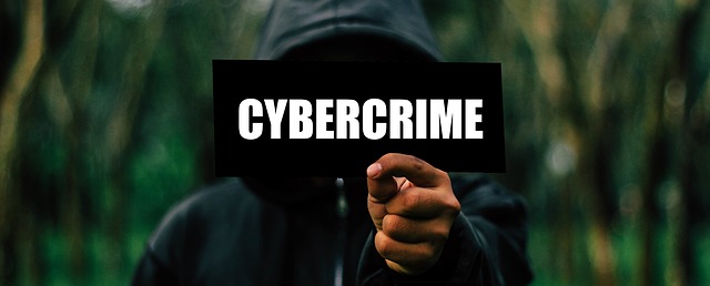Hacker in a black hoodie holding up a sign with 'Cybercrime' on it